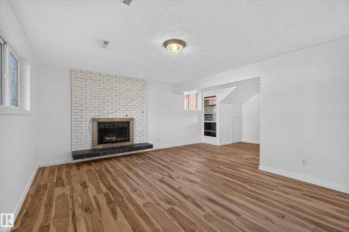White-painted brick fireplace with a dark stone hearth, wood-finish flooring, and built-in shelving - 13903 87 Street Nw, Edmonton, AB - Indoor Photo Showing Living Room With Fireplace