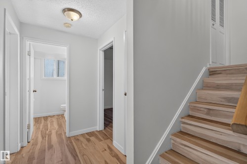 Wood-finish flooring throughout, bright white walls, flush-mount ceiling light, and natural wood staircase - 13903 87 Street Nw, Edmonton, AB - Indoor Photo Showing Other Room