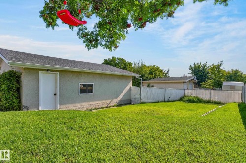 Expansive grassy area with a stucco exterior structure featuring a shingle roof, white door, and small window - 13903 87 Street Nw, Edmonton, AB - Outdoor