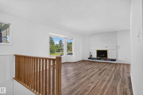 Bright interior with wood-finish flooring, a white brick fireplace, and large bay windows offering ample natural light - 13903 87 Street Nw, Edmonton, AB - Indoor Photo Showing Other Room With Fireplace