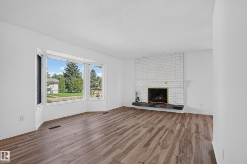 Expansive bay window, wood-finish flooring, white brick fireplace, dark hearth, and light-toned wall finishes - 13903 87 Street Nw, Edmonton, AB - Indoor Photo Showing Living Room With Fireplace
