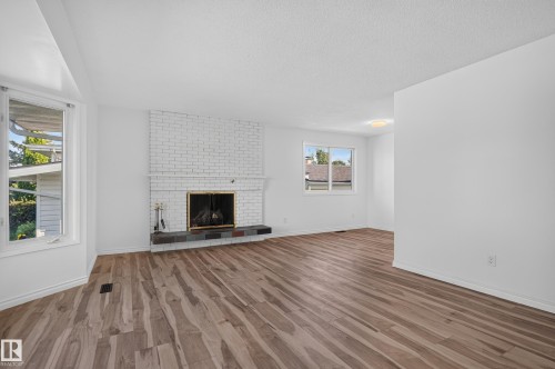Expansive living area featuring wood-finish flooring, a white-painted brick fireplace with a dark tile hearth, and abundant natural light from multiple windows - 13903 87 Street Nw, Edmonton, AB - Indoor Photo Showing Living Room With Fireplace