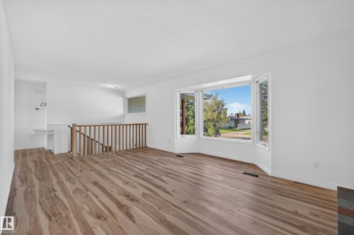 Spacious room featuring wood-finish flooring, a large bay window, and a wooden staircase railing - 13903 87 Street Nw, Edmonton, AB - Indoor Photo Showing Other Room