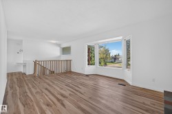 Spacious room featuring wood-finish flooring, a large bay window, and a wooden staircase railing - 