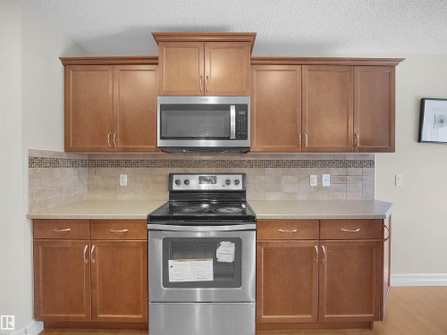 Wood-finish cabinetry with crown molding, stainless steel range and microwave, light-toned countertops, and mosaic tile backsplash - 17127 126 Street Nw, Edmonton, AB - Indoor Photo Showing Kitchen