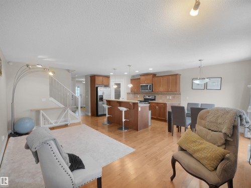 Light wood-finish flooring, staircase with white risers and handrail, kitchen island with counter seating, wood cabinetry, and stainless steel appliances - 17127 126 Street Nw, Edmonton, AB - Indoor