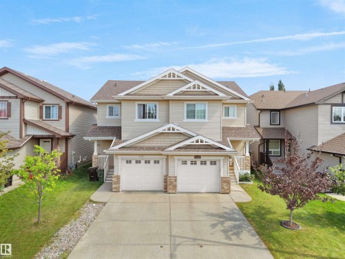 Duplex property featuring a neutral-toned exterior, gabled rooflines, two single-car garages, and concrete driveways - 17127 126 Street Nw, Edmonton, AB - Outdoor With Facade