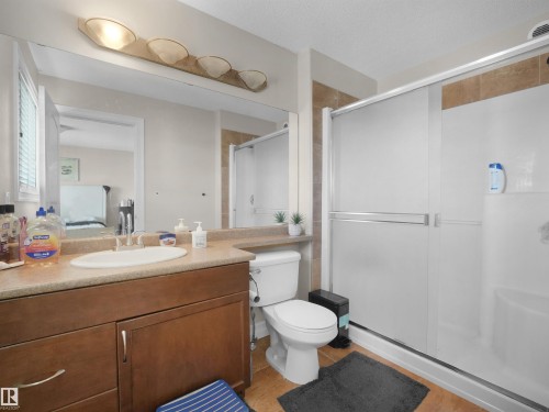 Bathroom featuring a wood-finish vanity with an integrated sink, a large mirror, and a shower with sliding doors - 17127 126 Street Nw, Edmonton, AB - Indoor Photo Showing Bathroom
