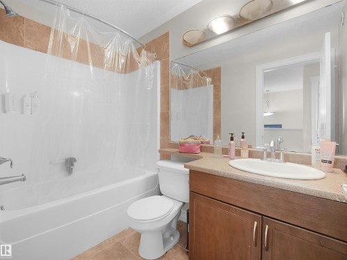Tub and shower combination with tile surround, wood-finish vanity with countertop, and an elongated mirror - 17127 126 Street Nw, Edmonton, AB - Indoor Photo Showing Bathroom