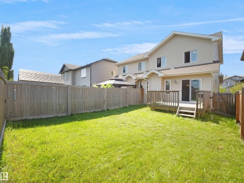 Expansive backyard featuring a manicured lawn, full privacy fence, and a wooden deck with a sliding glass door - 17127 126 Street Nw, Edmonton, AB - Outdoor