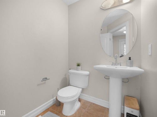 Ceramic tile flooring, pedestal sink, wall-mounted oval mirror, and a two-piece toilet - 17127 126 Street Nw, Edmonton, AB - Indoor Photo Showing Bathroom
