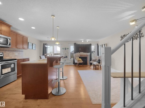 Open-concept living area with wood-finish flooring, a kitchen island, stainless steel appliances, and a fireplace with a mantel - 17127 126 Street Nw, Edmonton, AB - Indoor Photo Showing Kitchen
