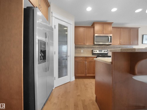 Stainless steel refrigerator, wood-finish flooring, wood cabinetry, stone-finish countertops, and recessed lighting - 17127 126 Street Nw, Edmonton, AB - Indoor Photo Showing Kitchen