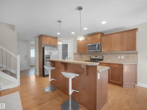 Open-concept kitchen featuring wood-finish cabinetry, stainless steel appliances, a breakfast bar, and wood-finish flooring - 17127 126 Street Nw, Edmonton, AB - Indoor Photo Showing Kitchen With Upgraded Kitchen