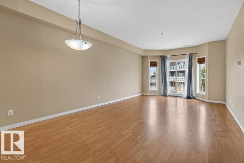 Expansive interior with wood-finish flooring, neutral-toned walls, and a contemporary semi-flush mount fixture - #205 4304 139 Av Nw, Edmonton, AB - Indoor