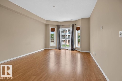 Wood-finish flooring throughout, light-toned wall paint, and a bay window configuration - #205 4304 139 Av Nw, Edmonton, AB - Indoor Photo Showing Other Room
