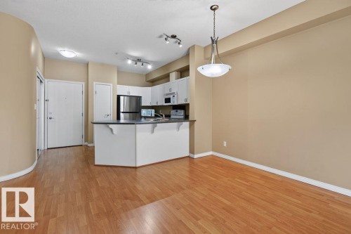 Kitchen with stainless steel appliances, white cabinetry, and a peninsula with countertop seating - #205 4304 139 Av Nw, Edmonton, AB - Indoor Photo Showing Kitchen