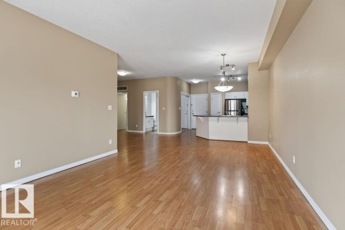 Wood-finish flooring throughout, neutral wall paint, kitchen with stainless steel appliances, kitchen island with counter seating, and overhead track lighting - #205 4304 139 Av Nw, Edmonton, AB - Indoor
