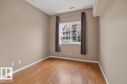 Wood-finish flooring, neutral wall tones, and a window with a building backdrop - #205 4304 139 Av Nw, Edmonton, AB - Indoor Photo Showing Other Room