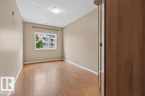 Wood-finish flooring, neutral wall paint, overhead flush-mount lighting, and a white-framed window - #205 4304 139 Av Nw, Edmonton, AB - Indoor Photo Showing Other Room