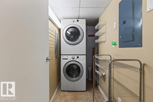 Compact laundry area featuring a stacked washer and dryer, tiled flooring, and neutral wall tones - #205 4304 139 Av Nw, Edmonton, AB - Indoor Photo Showing Laundry Room