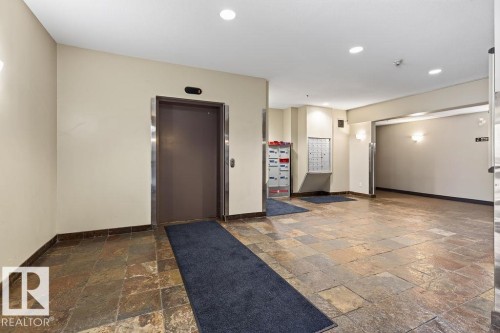 Spacious common area featuring natural stone tile flooring, recessed lighting, wall sconces, and a dedicated mail area - #205 4304 139 Av Nw, Edmonton, AB - Indoor Photo Showing Other Room
