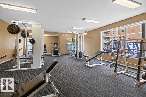 Fitness center featuring carpet flooring, large windows, and a variety of exercise equipment - #205 4304 139 Av Nw, Edmonton, AB - Indoor Photo Showing Gym Room