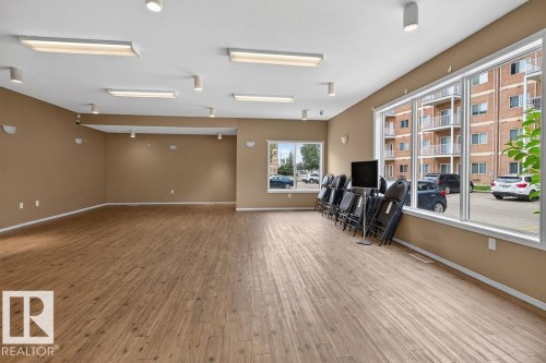Spacious room featuring wood-finish flooring, multiple large windows, and recessed lighting fixtures - #205 4304 139 Av Nw, Edmonton, AB - Indoor Photo Showing Other Room