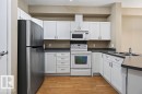 Kitchen featuring white shaker-style cabinetry, dark countertops, wood-finish flooring, and stainless steel appliances including a refrigerator, range, microwave, and double sink - #205 4304 139 Av Nw, Edmonton, AB  - Indoor Photo Showing Kitchen With Double Sink 