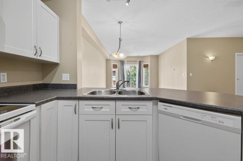 White cabinetry with chrome hardware, dual basin stainless steel sink, integrated dishwasher, and a bay window - #205 4304 139 Av Nw, Edmonton, AB - Indoor Photo Showing Kitchen With Double Sink