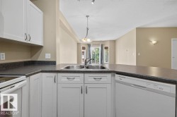 White cabinetry with chrome hardware, dual basin stainless steel sink, integrated dishwasher, and a bay window - 