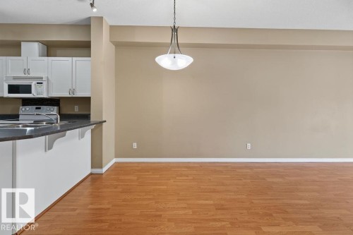 Wood-finish flooring, white cabinetry, dark stone-finish countertop, stainless-steel sink, and a pendant light fixture - #205 4304 139 Av Nw, Edmonton, AB - Indoor Photo Showing Kitchen With Double Sink