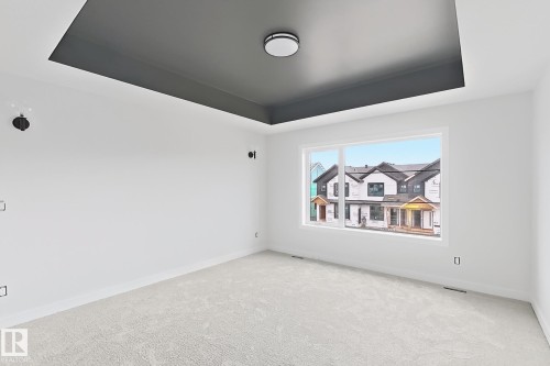 Tray ceiling with contrasting finish, contemporary flush mount lighting, white-painted walls, light-colored carpeting, and a large window - 13118 186 Avenue Nw, Edmonton, AB - Indoor Photo Showing Other Room