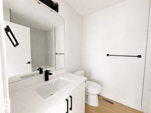 Vanity with integrated sink and matte black faucet, full-width mirror, white tiled shower enclosure, white toilet, and wood-finish flooring - 13118 186 Avenue Nw, Edmonton, AB - Indoor Photo Showing Bathroom