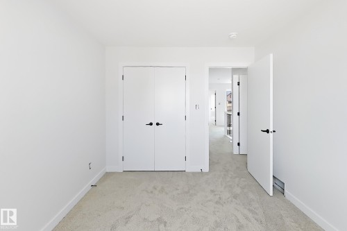 Light-toned carpet flooring, crisp white walls, white doors with matte black hardware, and an open doorway - 13118 186 Avenue Nw, Edmonton, AB - Indoor Photo Showing Other Room