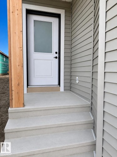 White exterior door with frosted glass insert, modern black door hardware, gray horizontal siding, wooden structural post, and concrete steps - 13118 186 Avenue Nw, Edmonton, AB - Outdoor With Exterior