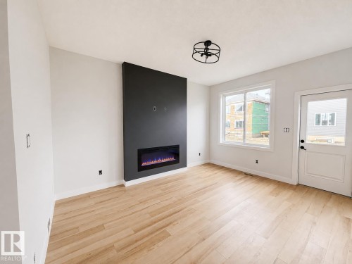 Contemporary electric fireplace with a dark accent wall, light wood-finish flooring, and a modern semi-flush mount ceiling fixture - 13118 186 Avenue Nw, Edmonton, AB - Indoor With Fireplace