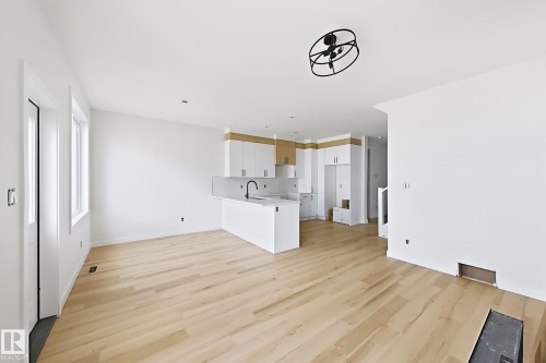 Light wood-finish flooring throughout, modern kitchen cabinetry with wood accents, integrated sink with matte black faucet, and white countertops - 13118 186 Avenue Nw, Edmonton, AB - Indoor