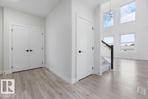 Wood-finish flooring, white walls, white doors with matte black hardware, and a staircase with glass panel railing - 9331 181 Avenue Nw, Edmonton, AB - Indoor Photo Showing Other Room