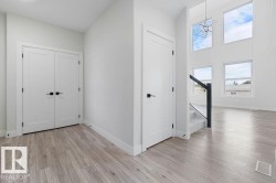 Wood-finish flooring, white walls, white doors with matte black hardware, and a staircase with glass panel railing - 