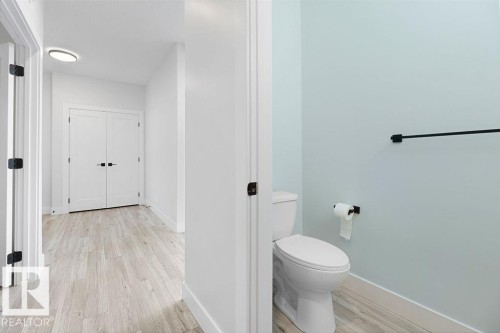 Light wood-finish flooring extending into a private water closet with a white toilet and light blue walls - 9331 181 Avenue Nw, Edmonton, AB - Indoor Photo Showing Bathroom