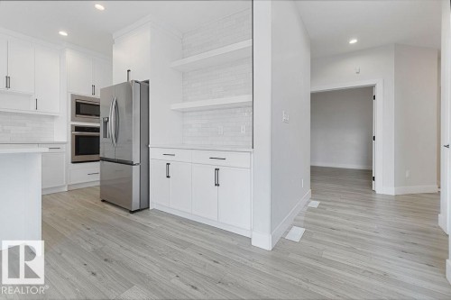 Contemporary kitchen featuring white cabinetry, stainless steel appliances, light wood-finish flooring, and open shelving - 9331 181 Avenue Nw, Edmonton, AB - Indoor Photo Showing Kitchen