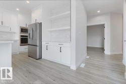 Contemporary kitchen featuring white cabinetry, stainless steel appliances, light wood-finish flooring, and open shelving - 
