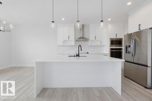 Kitchen featuring a large center island, stainless steel appliances, white cabinetry, a tile backsplash, and wood-finish flooring - 9331 181 Avenue Nw, Edmonton, AB - Indoor Photo Showing Kitchen With Upgraded Kitchen
