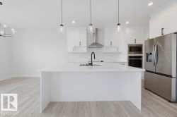 Kitchen featuring a large center island, stainless steel appliances, white cabinetry, a tile backsplash, and wood-finish flooring - 