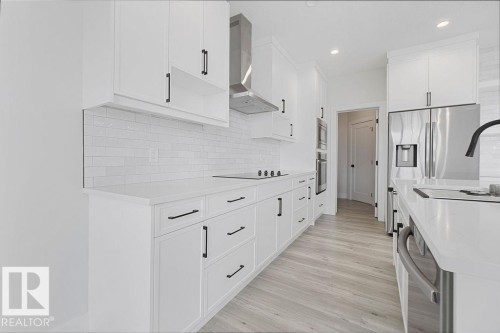 White shaker-style cabinetry with matte black hardware, subway tile backsplash, stainless steel appliances, light wood-finish flooring, and recessed lighting - 9331 181 Avenue Nw, Edmonton, AB - Indoor Photo Showing Kitchen With Upgraded Kitchen