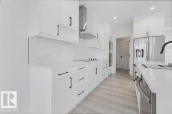 White shaker-style cabinetry with matte black hardware, subway tile backsplash, stainless steel appliances, light wood-finish flooring, and recessed lighting - 