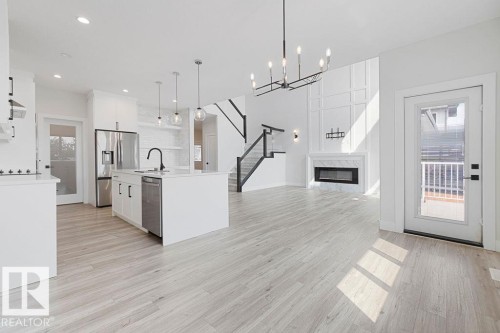 Open-concept living space with light wood-finish flooring, a contemporary fireplace with a marble-finish surround, and a modern chandelier - 9331 181 Avenue Nw, Edmonton, AB - Indoor Photo Showing Kitchen With Upgraded Kitchen