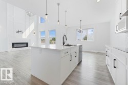 Open-concept living space with wood-finish flooring, a kitchen island with pendant lighting, white cabinetry, and a fireplace with a marble-style surround - 