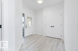 Light wood-finish flooring, white walls, and a ceiling-mounted light fixture illuminate the entry area - 
